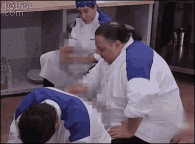 a group of chefs are working in a kitchen and one of them is kneeling on the floor .