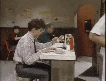 a man sits at a table in a restaurant with a sign that says pizza pie slices on the wall behind him