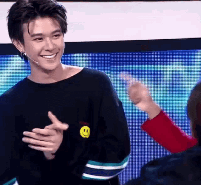 a young man wearing a black sweater with a smiley face on it is smiling
