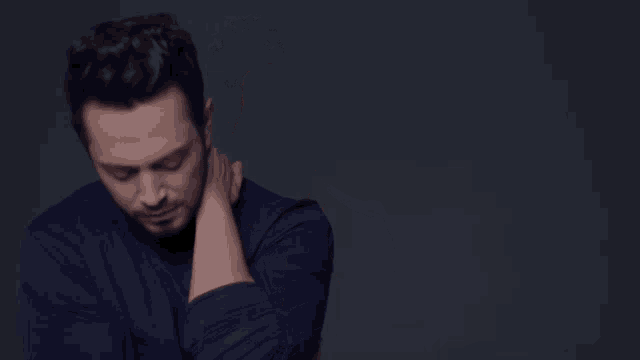 a man in a blue shirt is holding his neck in pain