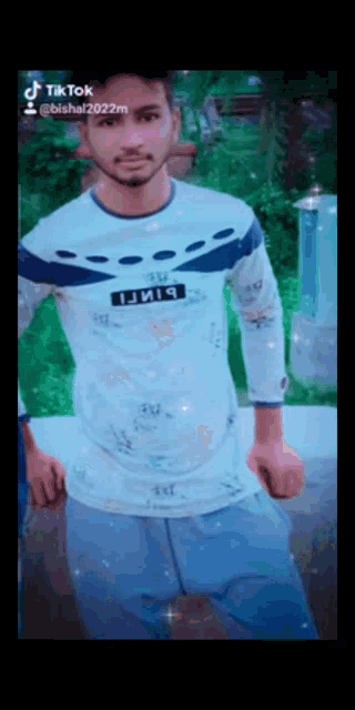 a man wearing a white shirt with a blue stripe on the sleeve is standing in a park