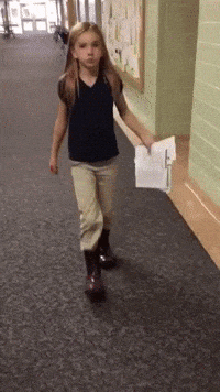 a little girl walking down a hallway holding a folder