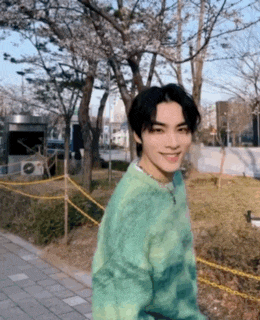 a young man wearing a green sweater is standing in front of a park