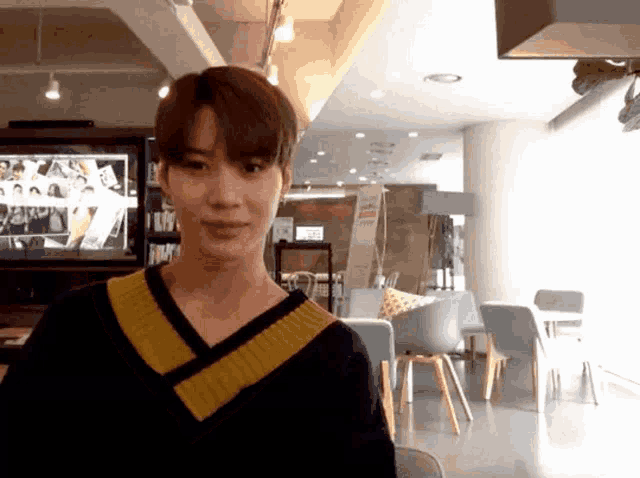 a young man wearing a yellow and black sweater is standing in a room