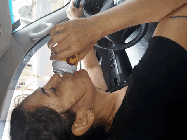 a woman in a car drinking from a can that says ' coca-cola ' on it