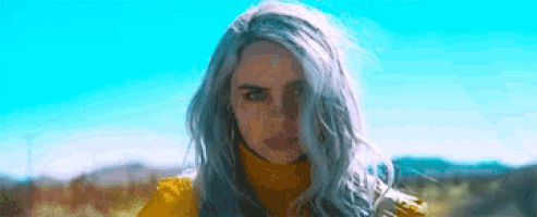 a woman with gray hair and a yellow jacket is standing in a field .