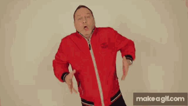 a man in a red jacket is making a funny face with his hands in the air .