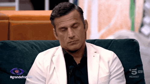 a man in a white jacket sits on a couch in front of a sign that says 5 hd