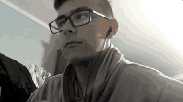 a man wearing glasses and ear buds looks at the camera