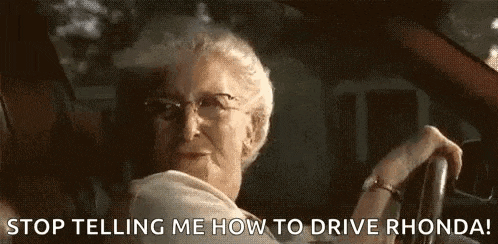 an elderly woman is driving a car and talking to another person .