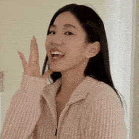 a woman wearing a pink sweater is smiling and covering her mouth with her hands .