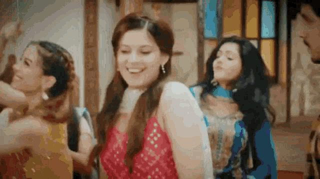 a group of women are dancing together in a room . one of the women is wearing a red top .