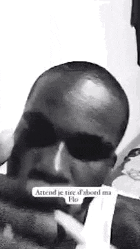 a black and white photo of a bald man wearing sunglasses and a white shirt .