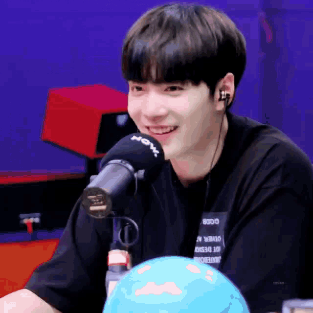 a young man wearing headphones and a black shirt is sitting in front of a microphone and smiling .