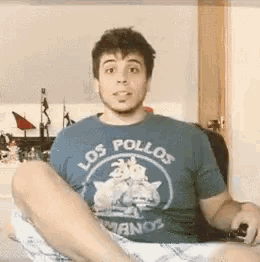 a man wearing a los pollos shirt is sitting on the floor