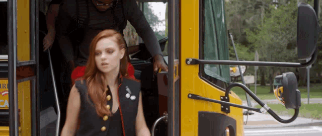 a woman with red hair is getting off a yellow bus with the letter r on the side