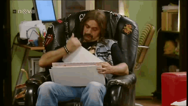 a man is sitting in a chair with papers in front of a tv screen that says nova on it