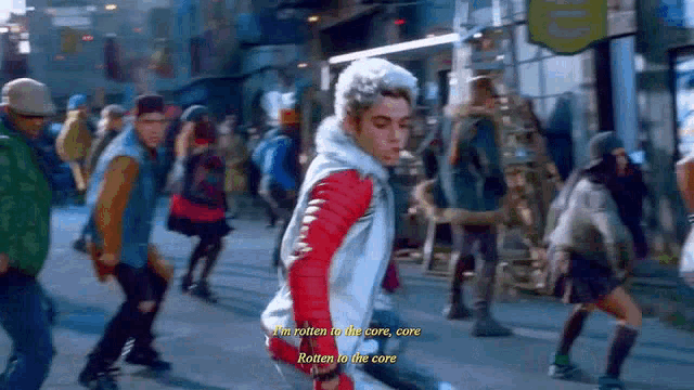 a man in a red jacket is walking down a street with a crowd of people .