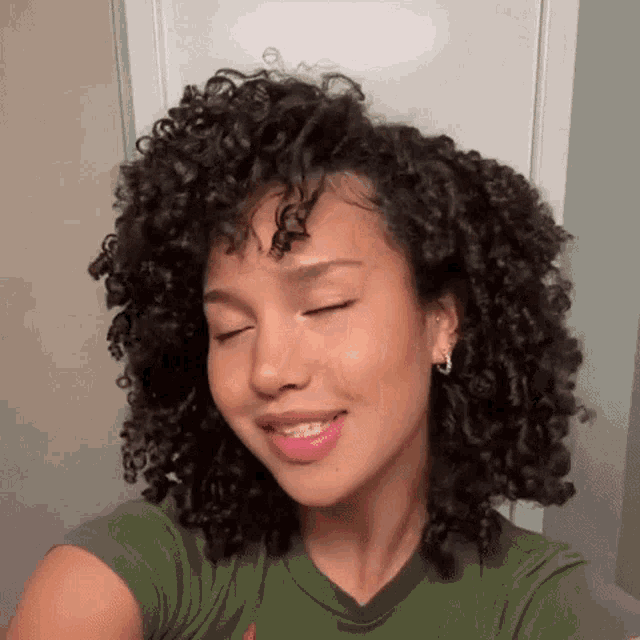 a woman with curly hair is taking a selfie with her eyes closed and wearing braces .
