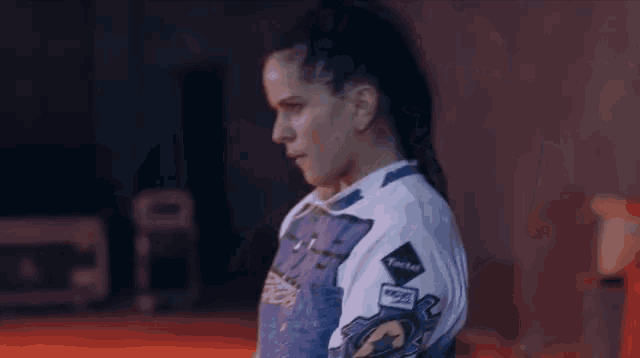 a woman with dreadlocks is standing in a dark room wearing a purple shirt .