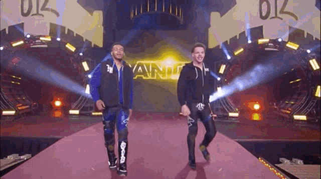 two men are walking down a red carpet on a stage with a sign that says yanu in the background .
