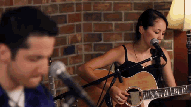 a woman singing into a microphone next to a man playing a guitar