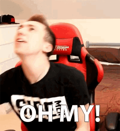 a man in a black shirt is sitting in a red gaming chair and says oh my !