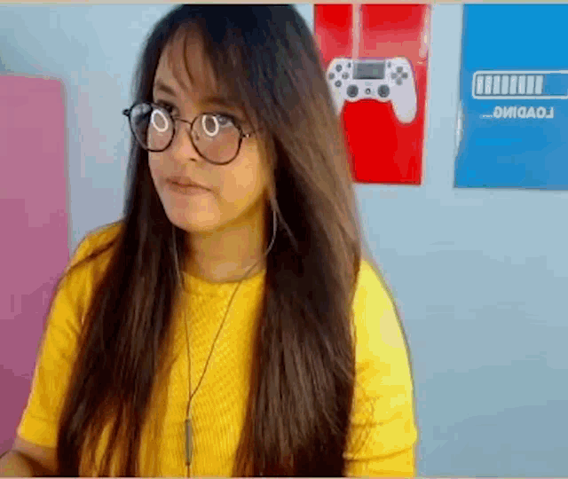 a woman wearing glasses and a yellow shirt is sitting in front of a video game controller .