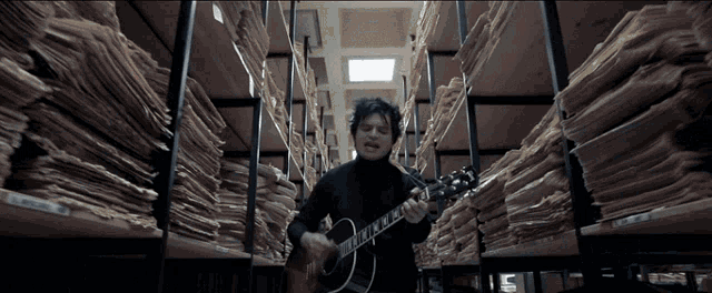 a man is playing a guitar in a room filled with shelves of papers