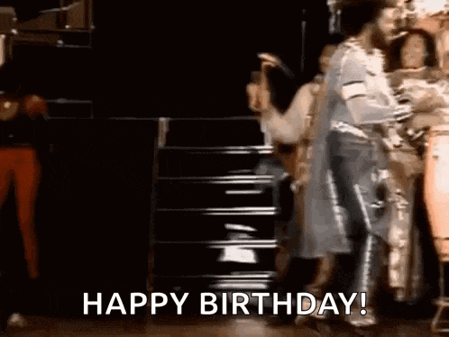 a group of people are dancing on a stage and the words `` happy birthday '' are being displayed .