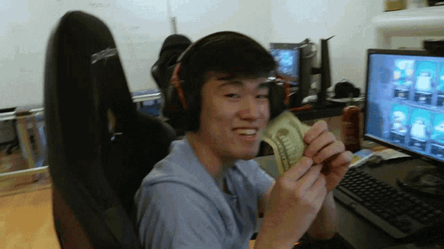 a man wearing headphones holds a dollar bill in front of a computer screen