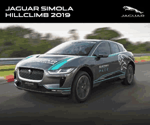 a jaguar simola is driving on a road with trees in the background