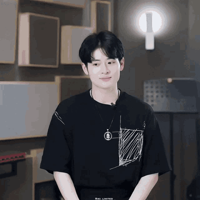 a young man wearing a black t-shirt and a necklace with the word riki limited on the bottom