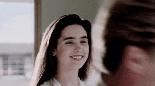 a woman with long hair is smiling at a man in a room .