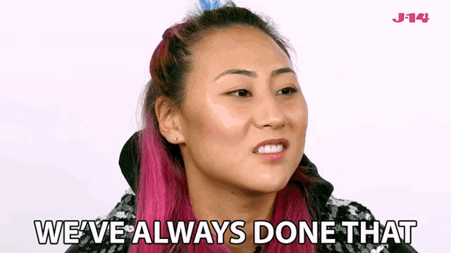a woman with pink hair is making a face and says we 've always done that