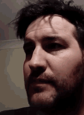 a man with a beard looks at the camera with his eyes closed