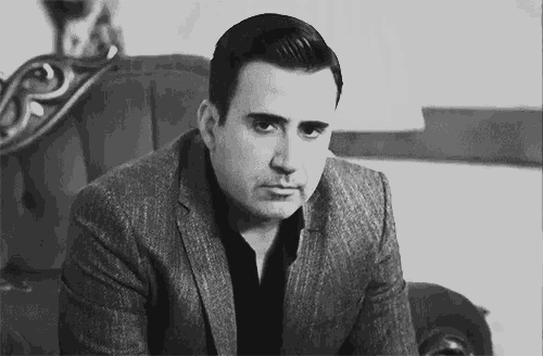 a man in a suit is sitting on a couch looking at the camera