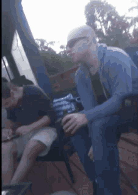a man wearing sunglasses sits on a chair while another man sits next to him