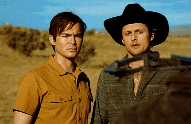 two men wearing cowboy hats are standing in a field