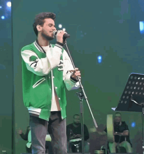 a man singing into a microphone wearing a green varsity jacket