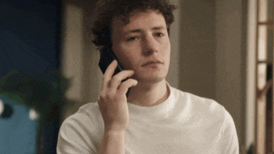 a young man with curly hair is talking on his cell phone