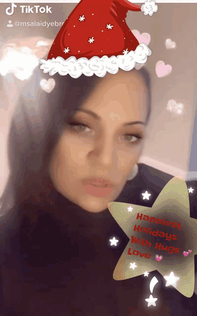 a woman wearing a santa hat and a star with the words happiest holidays with hugs on it