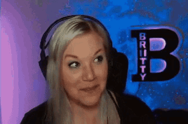 a blonde woman wearing headphones is smiling in front of a sign that says britty b