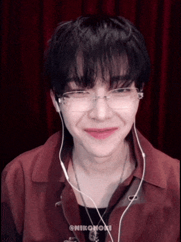 a young man wearing glasses and earbuds is smiling .