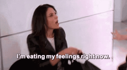 a woman is sitting at a table with her mouth open and says `` i 'm eating my feelings right now . ''