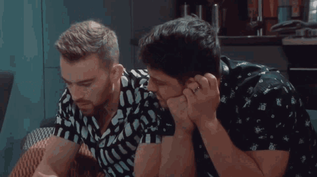 two men are sitting next to each other and one has a ring in his finger