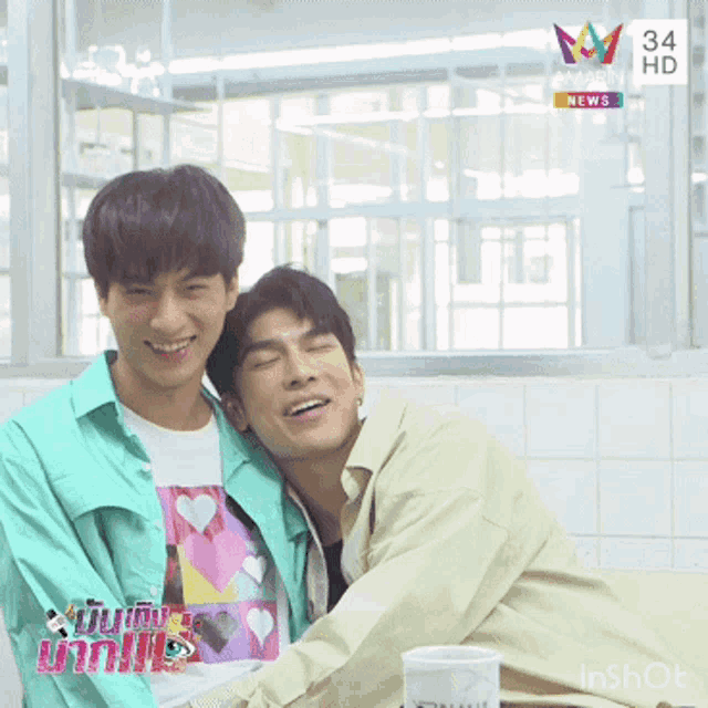 two young men are hugging and smiling in front of a screen that says 34 hd