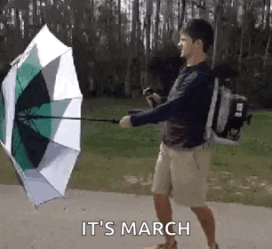 a man is holding an umbrella in the wind with the words `` it 's march '' written on the bottom .