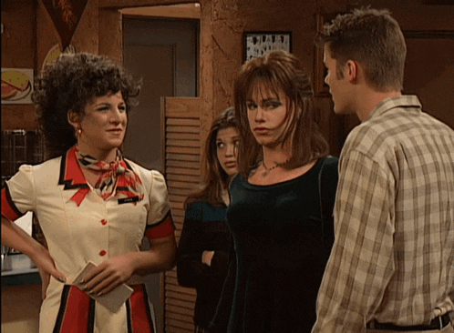 a man in a plaid shirt stands between two women in a restaurant