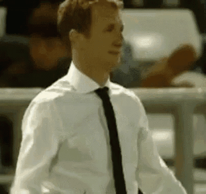 a man in a white shirt and black tie is standing in front of a fence .